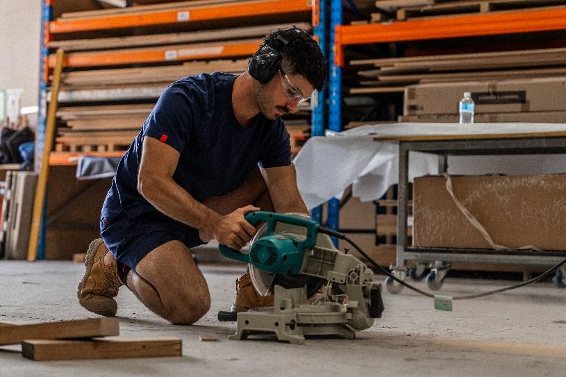 A person in a blue shirt and goggles using a circular saw

Description automatically generated
