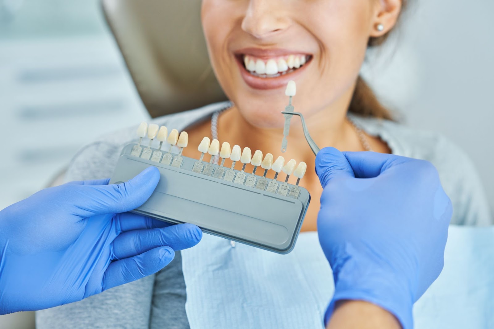 hand of a dentist holding teeth samples for a female patient smiling for dental crowns