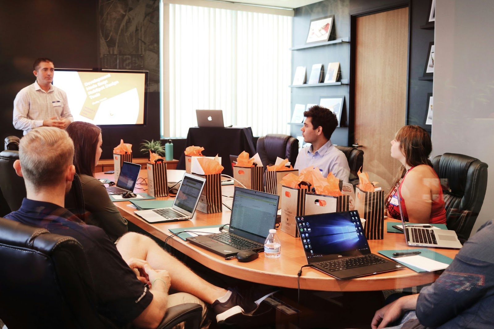 Personas en una sala de conferencias participando en una presentación, con laptops y materiales de trabajo sobre la mesa
