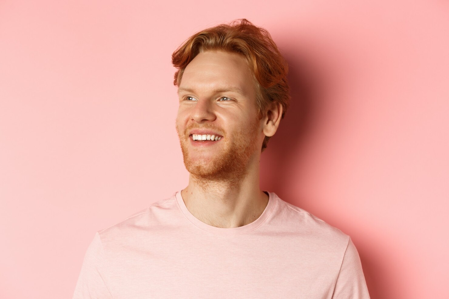 A man looks away and laughs in a pink shirt.