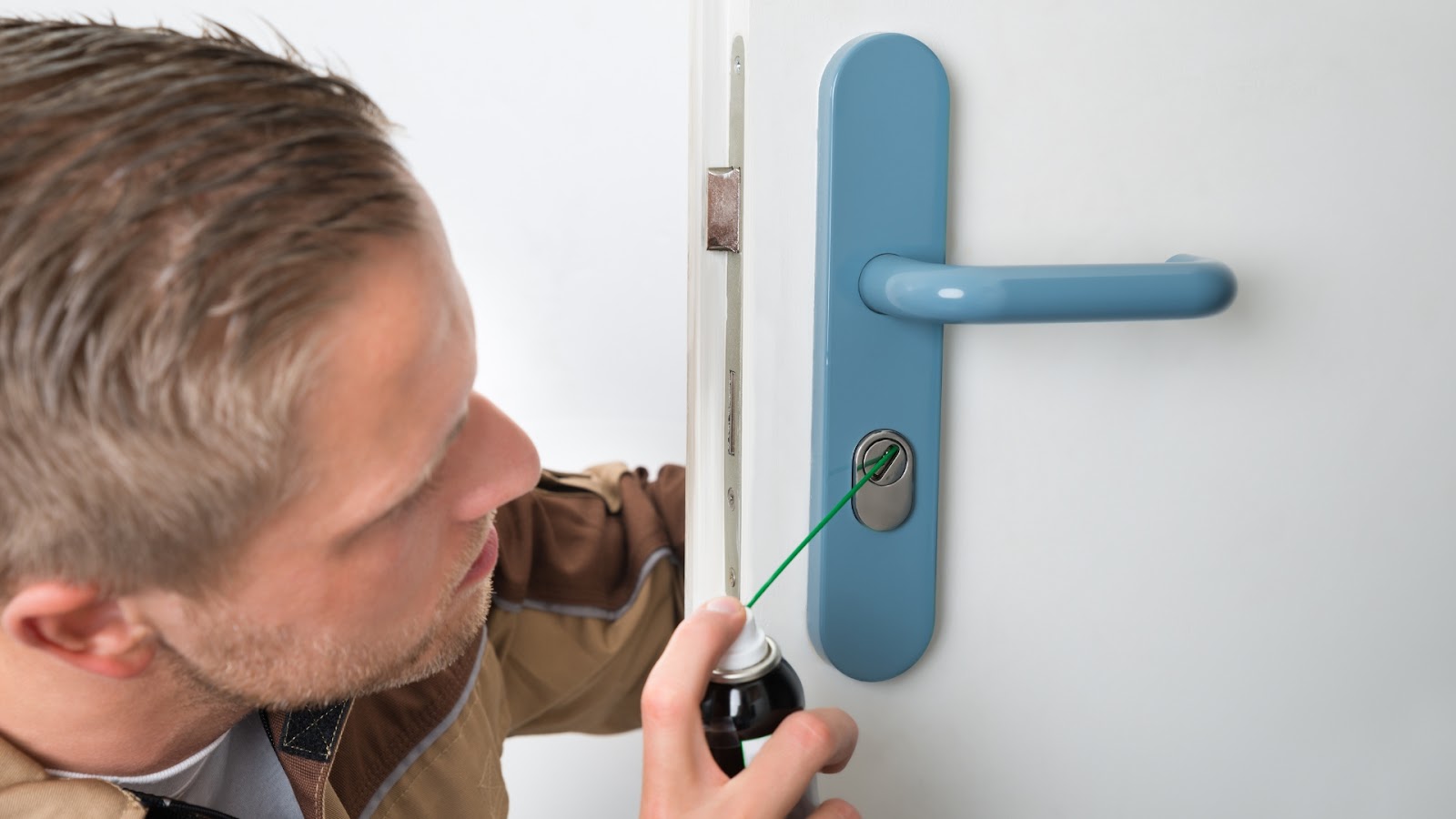 A locksmith applies lubricant to the keyhole of a front door lock to ensure smooth operation.