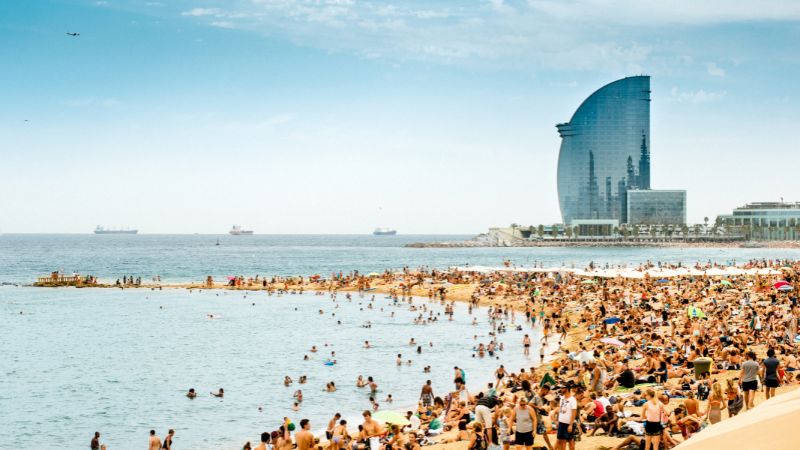 Barcelona beachfront packed with sunseekers alongside a curved high-rise.