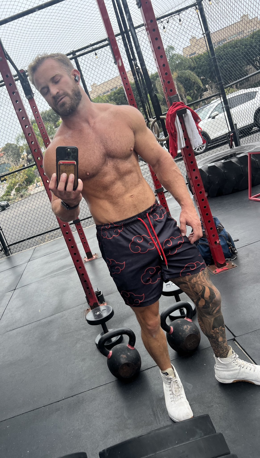 Bruce Jones taking a gay shirtless selfie in an outdoor gym surrounded by weights and kettlebells