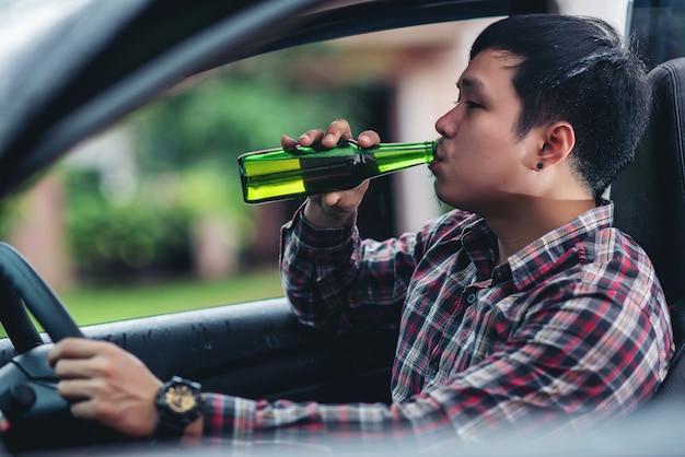Free photo asian man holds a beer bottle while is driving a car