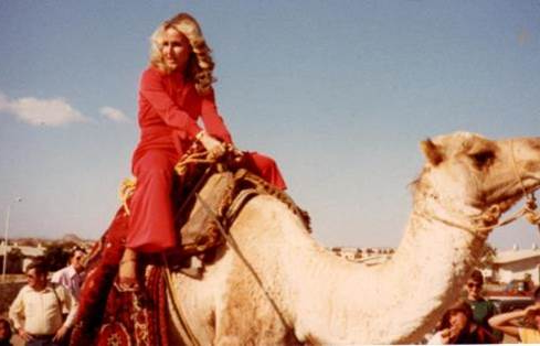 A person in red dress riding a camel

Description automatically generated