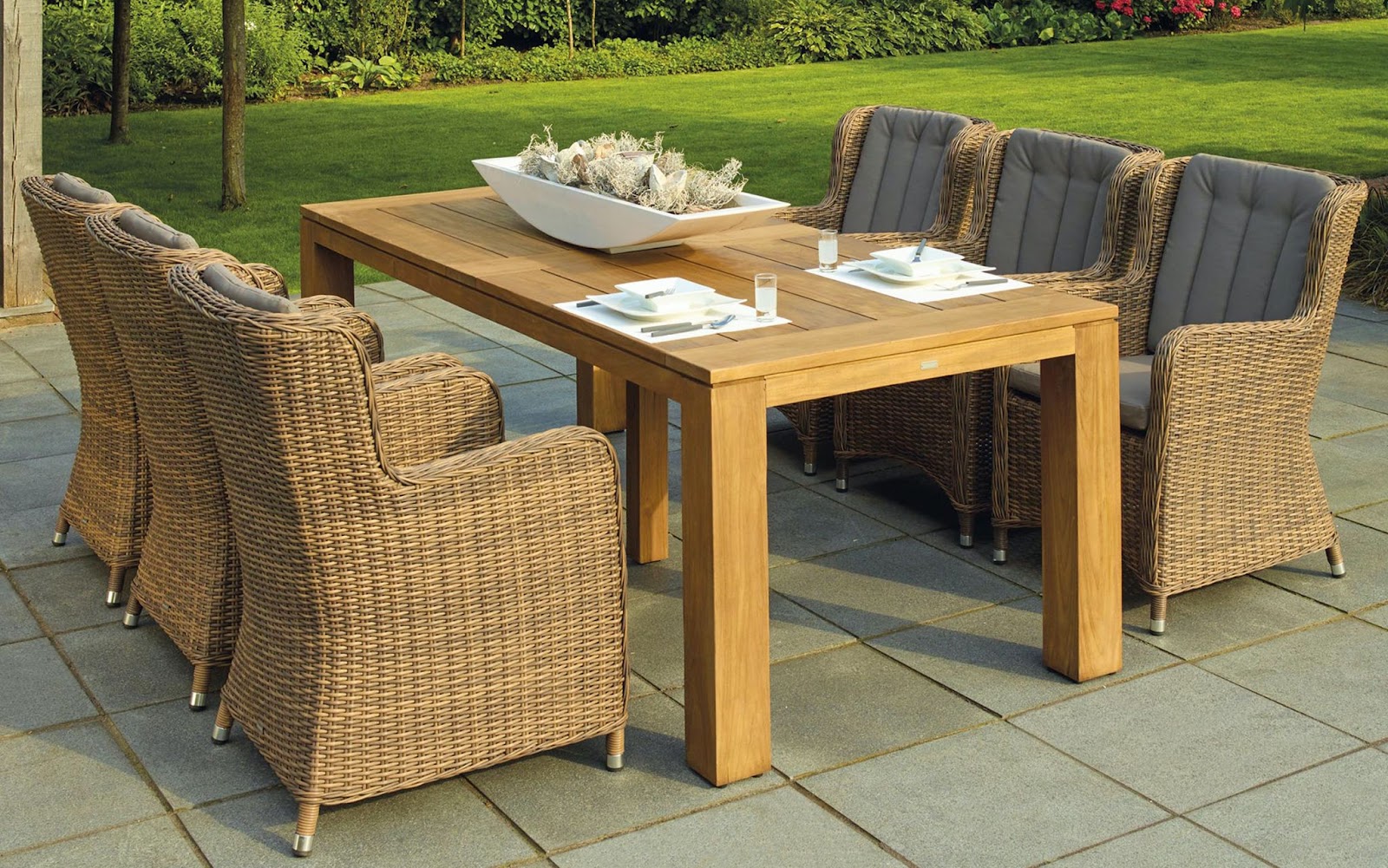 wooden outdoor dining table with cushioned wicker chair on stone tile patio