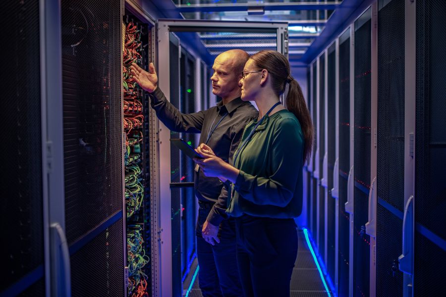 Two people in a server room, focused on a computer.