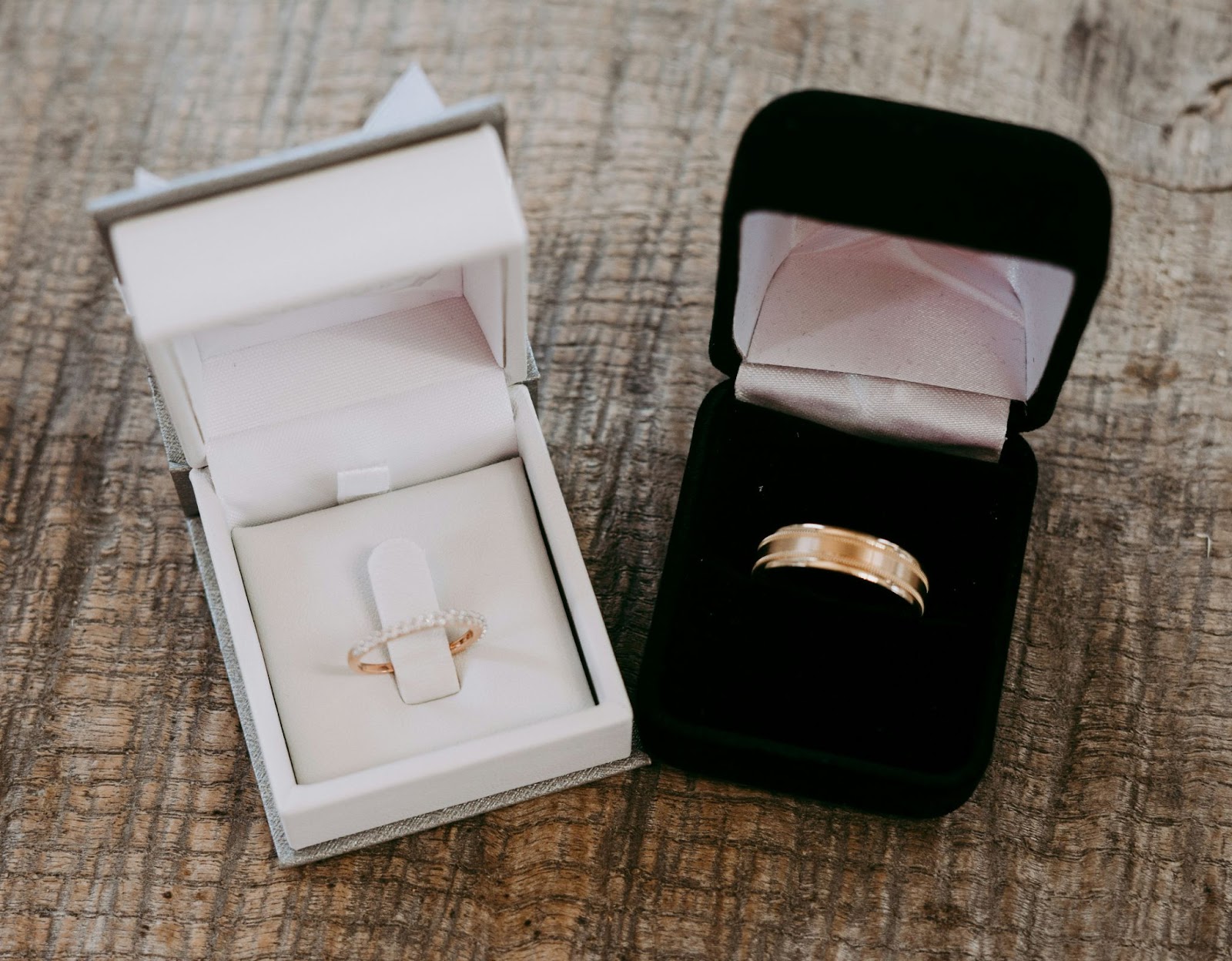 Matching gold wedding band set in their ring boxes on a wood table.