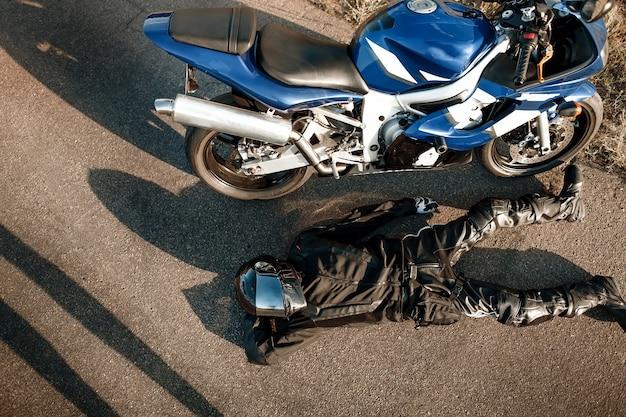 Photo motorcyclist in leather protective suit and a black helmet lies on the asphalt near a sports motorcycle. biker in black on the road. view from above