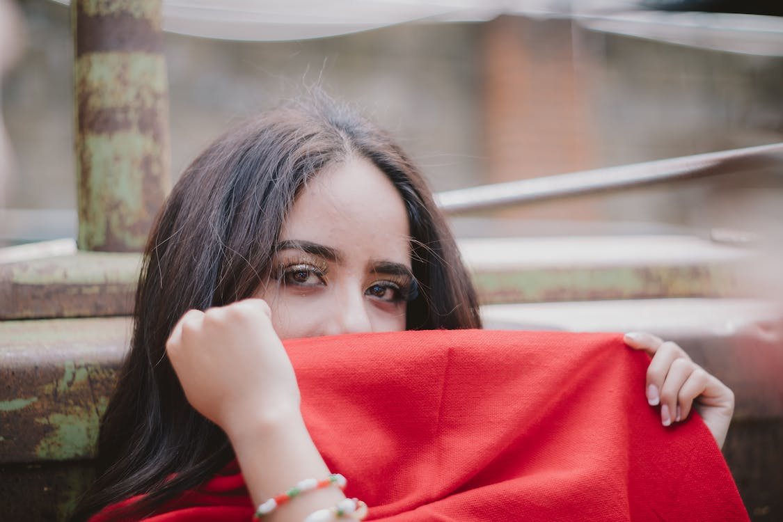 a woman covering her mouth using the red fabric of her scarf