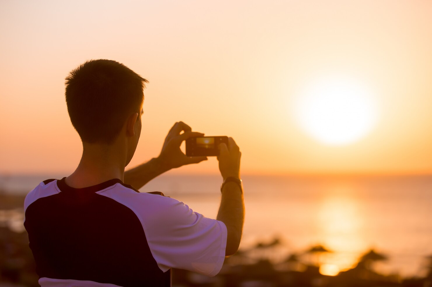 A man taking a photo of the sea at sunset. 