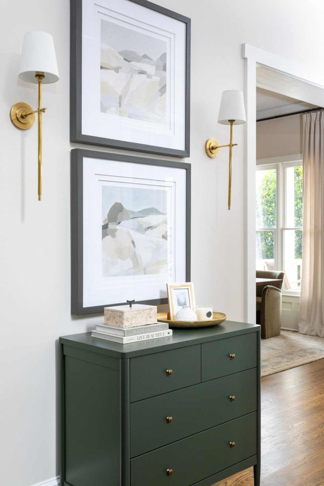 Green sideboard with wall sconces and landscape artwork. 