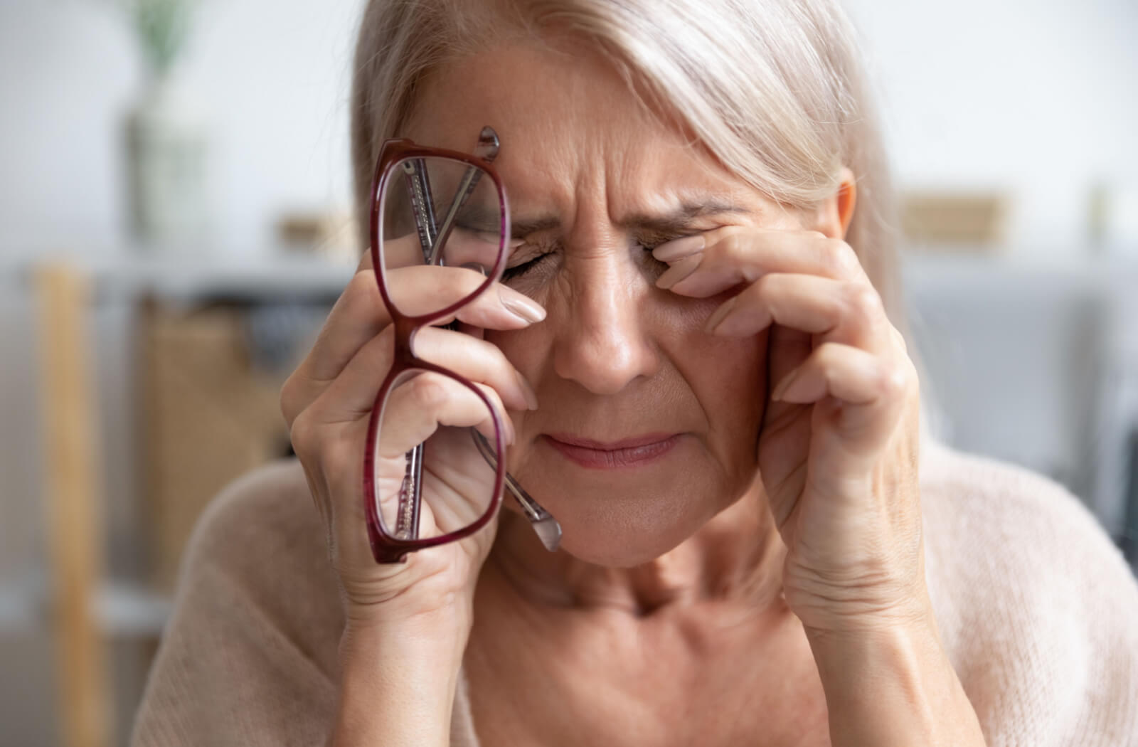 An older adult woman experiencing eye pain that is possibly caused by glaucoma.