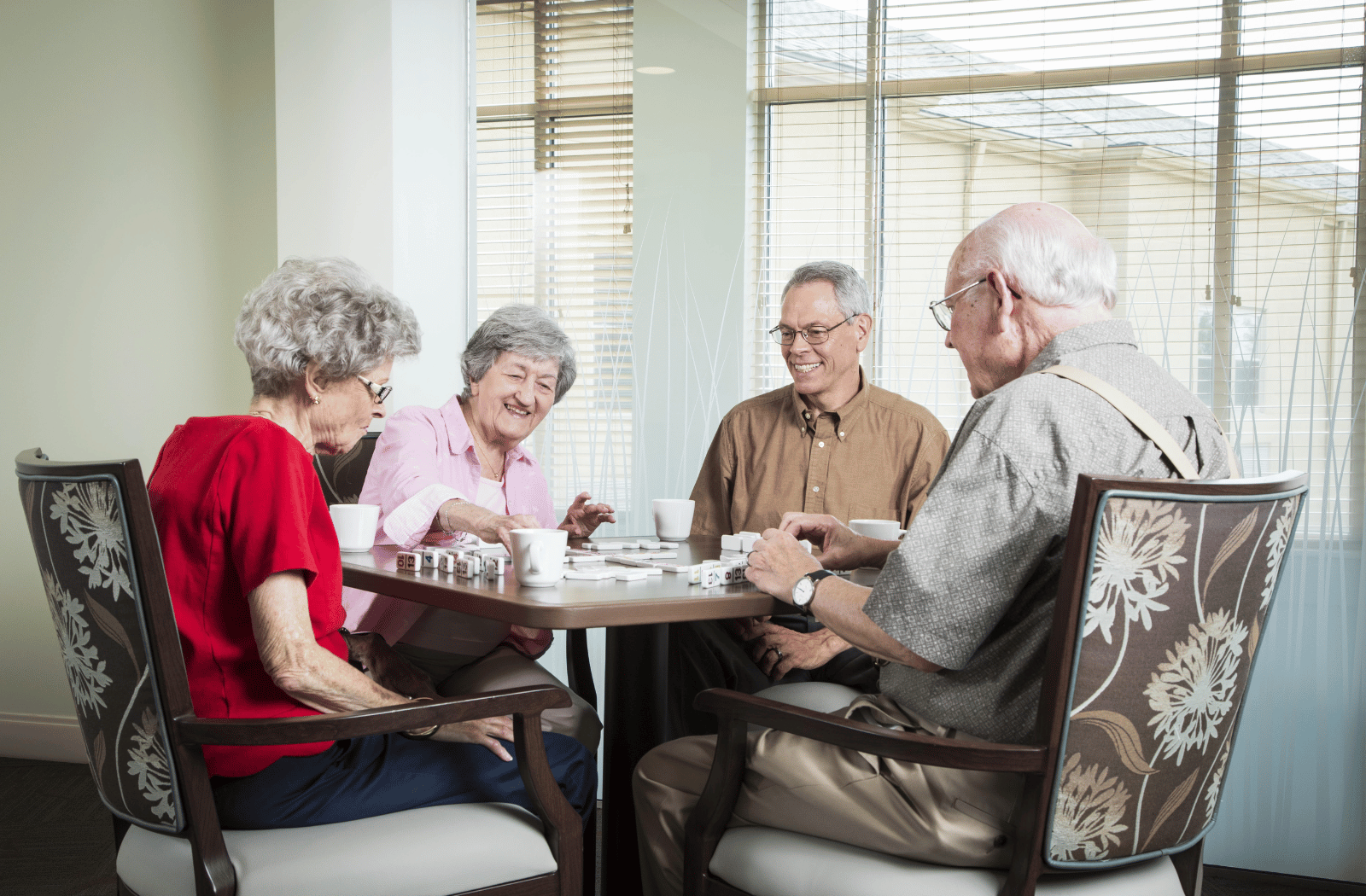 A group of senior living residents drinking coffee together and playing a game of dominoes 