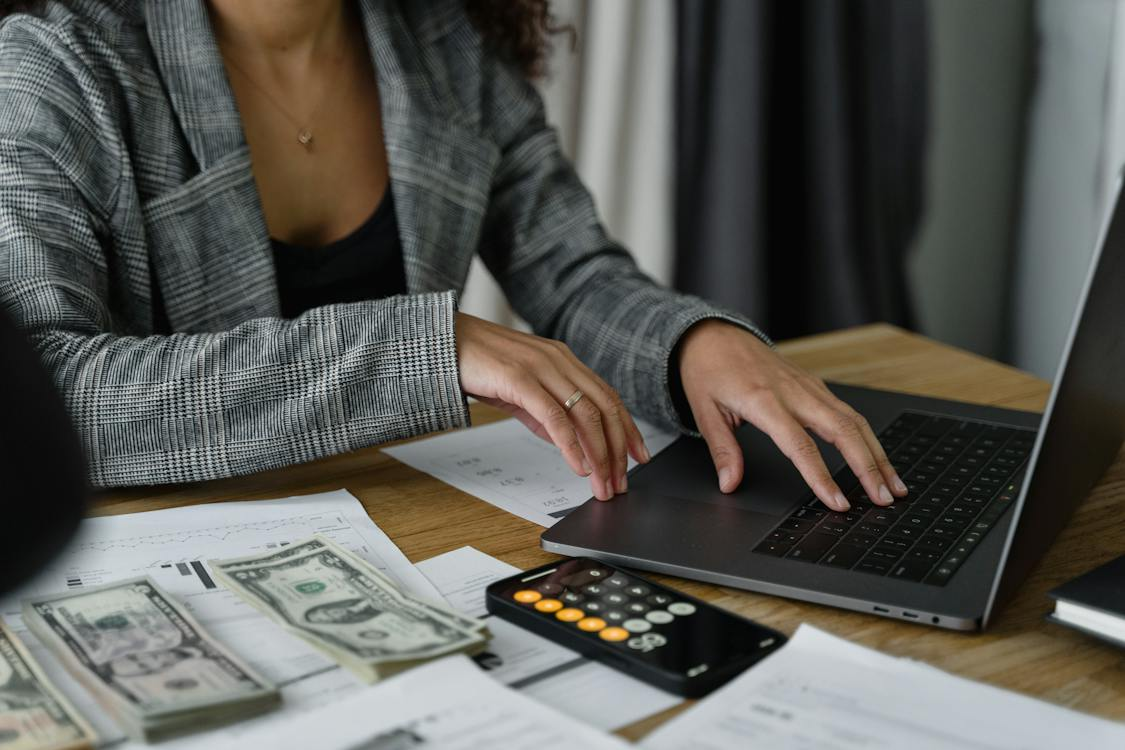 A woman on laptop with cash and a calculator