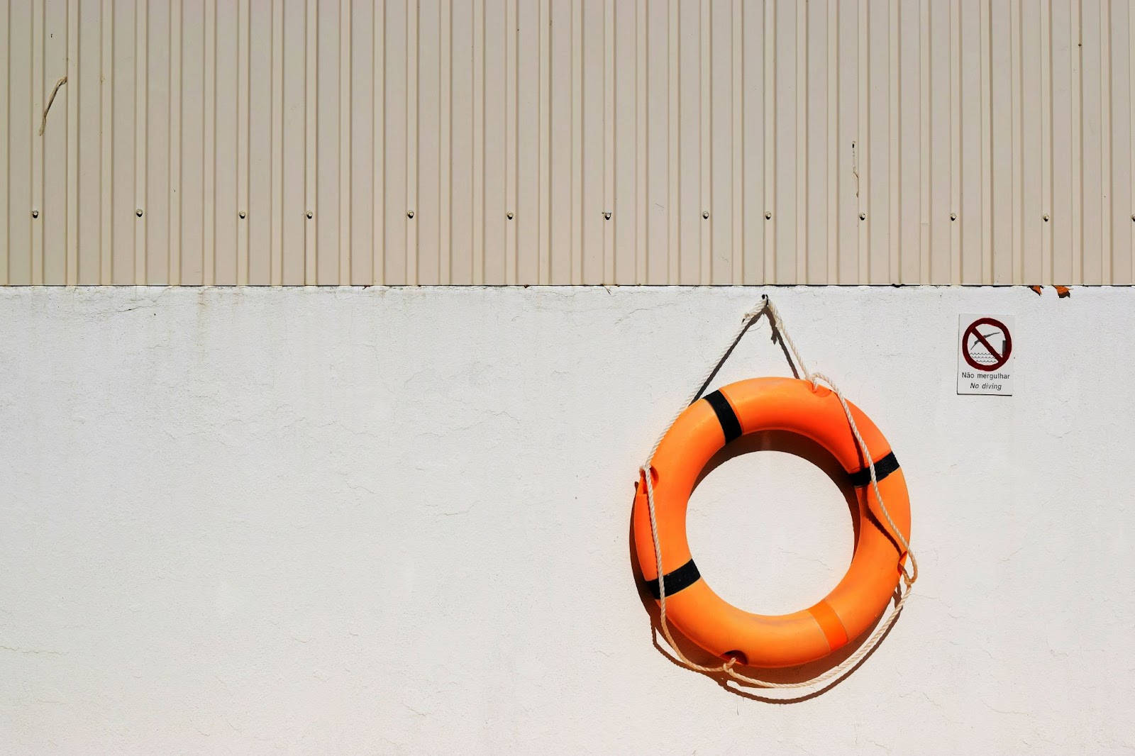 A bright orange life buoy hanging on a while wall beside a 'no diving' sign