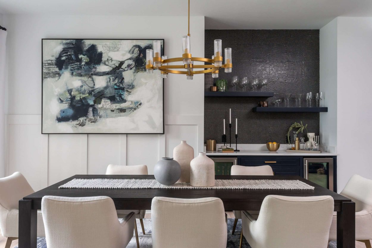Dining room with gold chandelier, black bar area, abstract blue art, and rectangular table. 