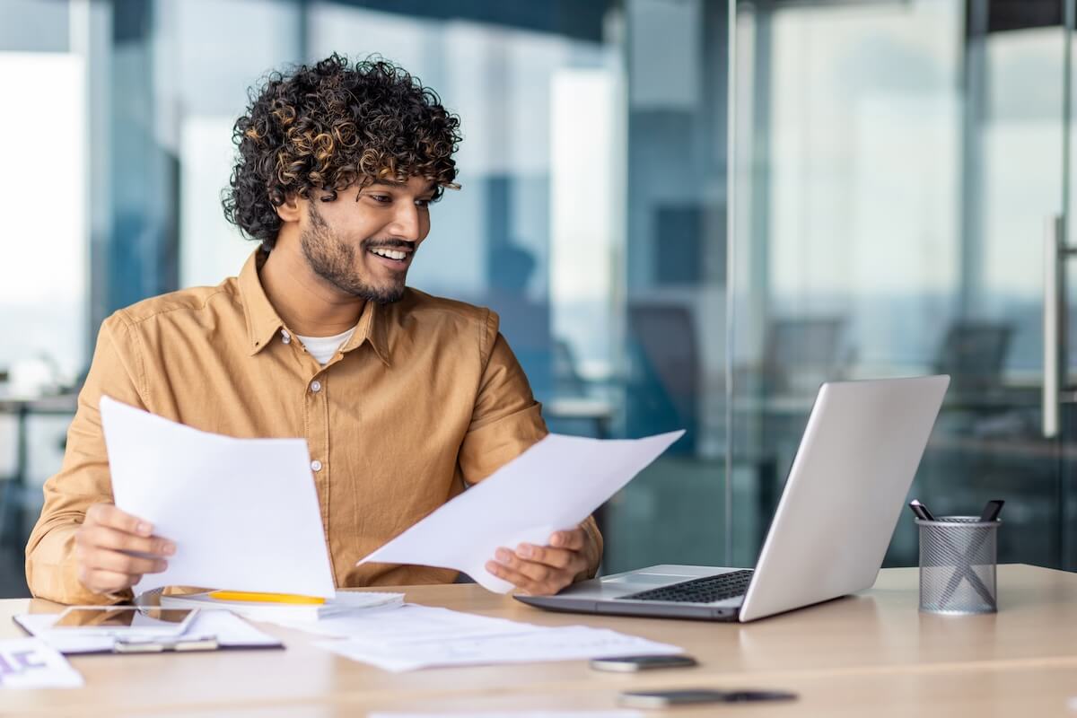 Behavioral health revenue cycle management: entrepreneur holding some documents while looking at a laptop