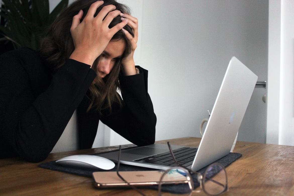 a stressed out woman staring closely at her laptop with her hands on her head