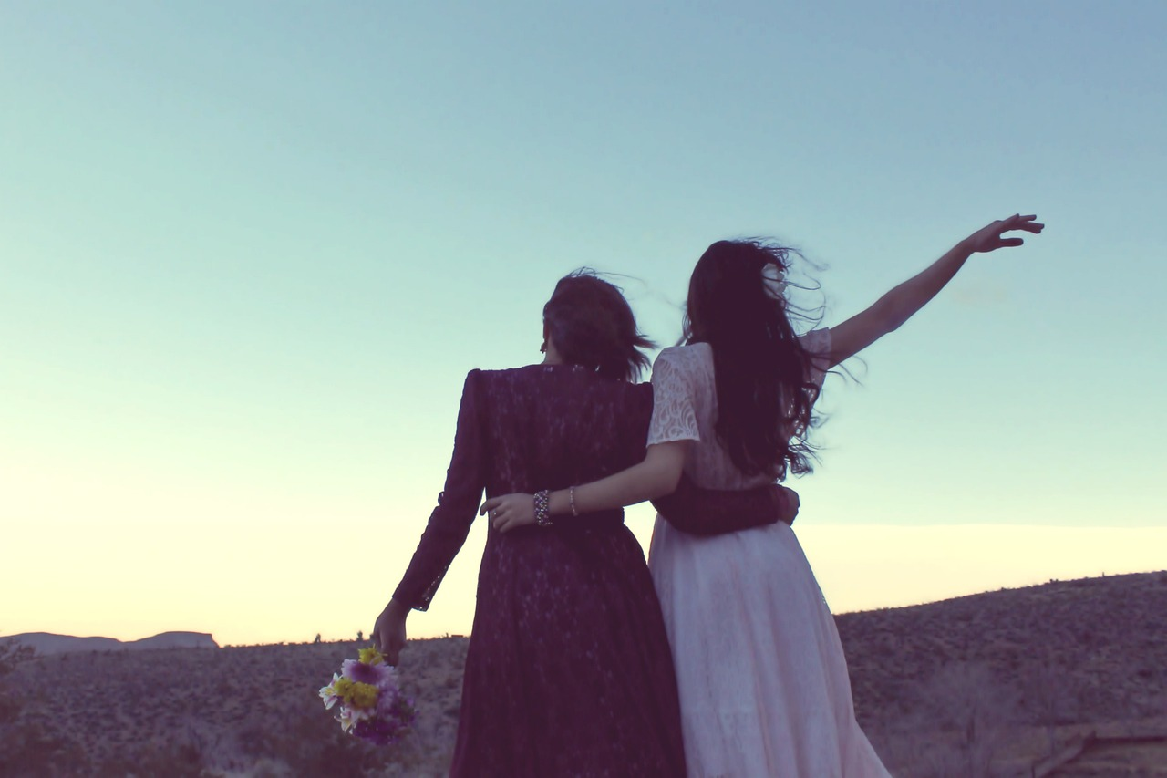 Back view of two women, arms round each other’s waist, looking at evening sky – spending quality time together