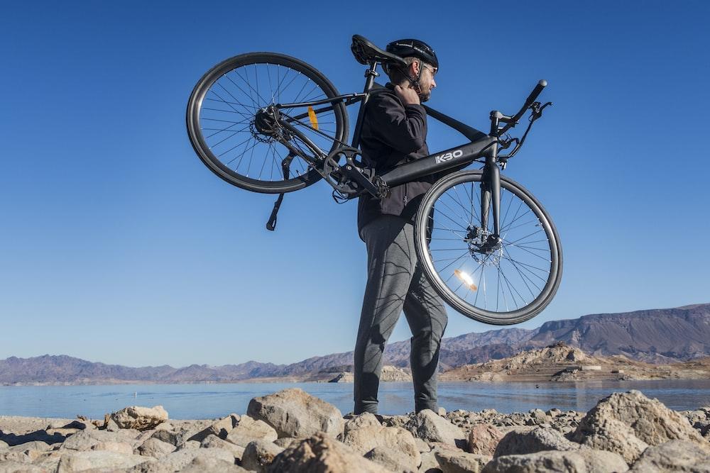 man in blue denim jacket and gray pants holding black mountain bike