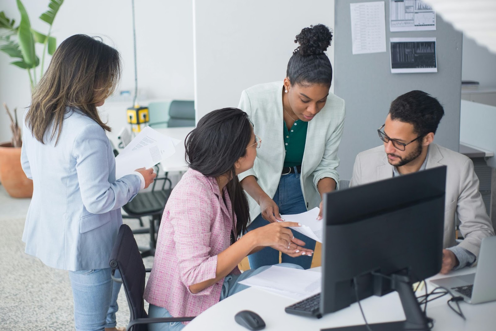 A group of people gathered at a computer workstation having a discussion