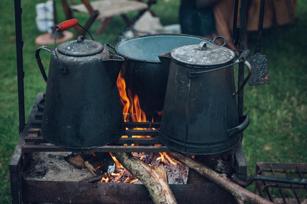 two kettles and one pot on top of fire