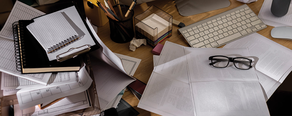 A cluttered office desk filled with piles of papers