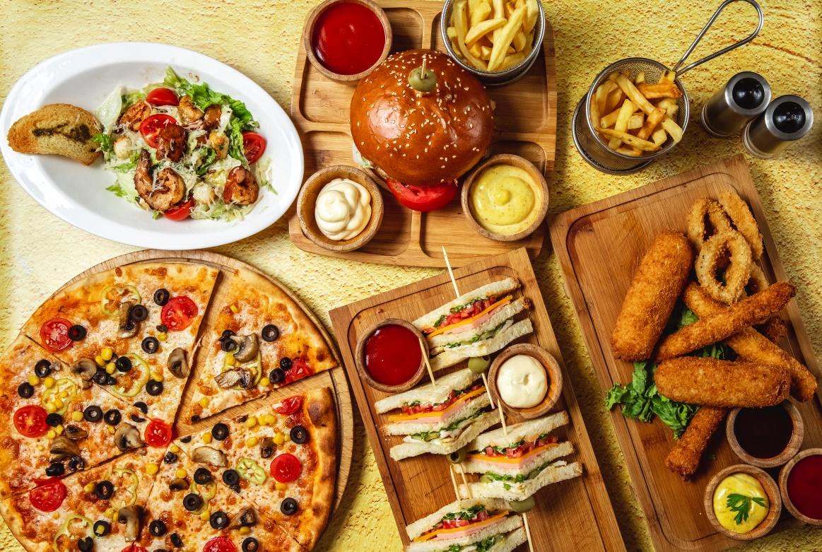 top-view-fast-food-mix-mozzarella-sticks-club-sandwich-hamburger-mushroom-pizza-caesar-shrimp-salad-french-fries-ketchup-mayo-cheese-sauces-table