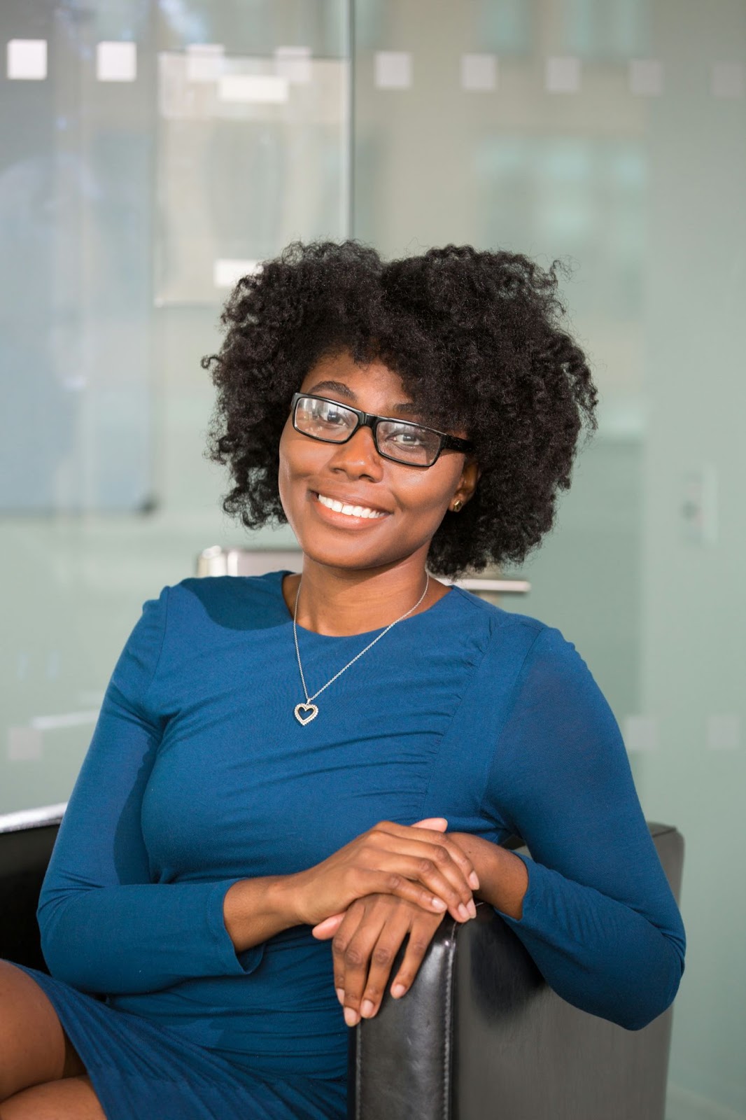 A woman with spectacles is sitting on a chair to pose for her professional headshots.