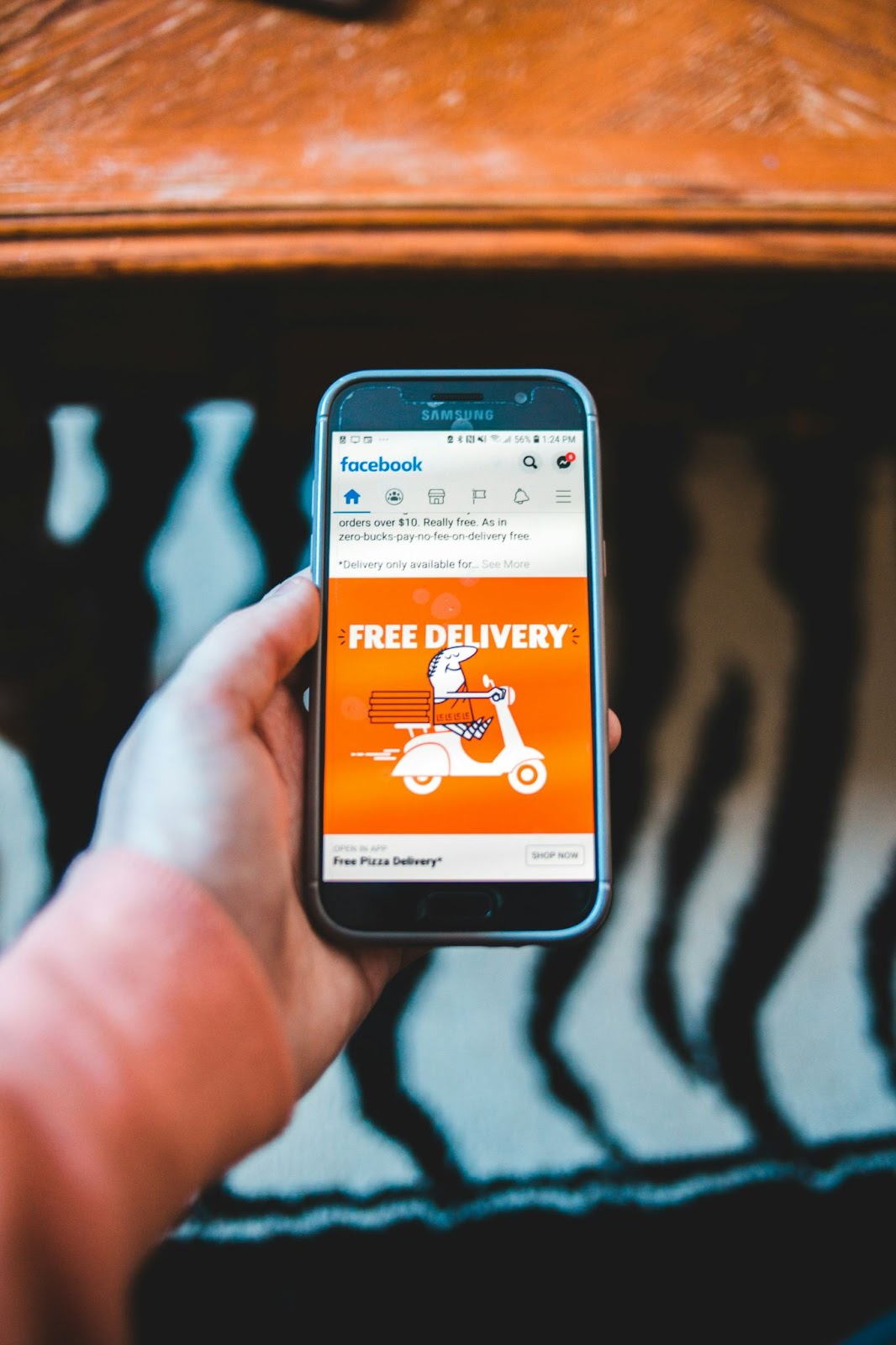 A person holding a phone and showing an ad for free delivery on Facebook’s feed.