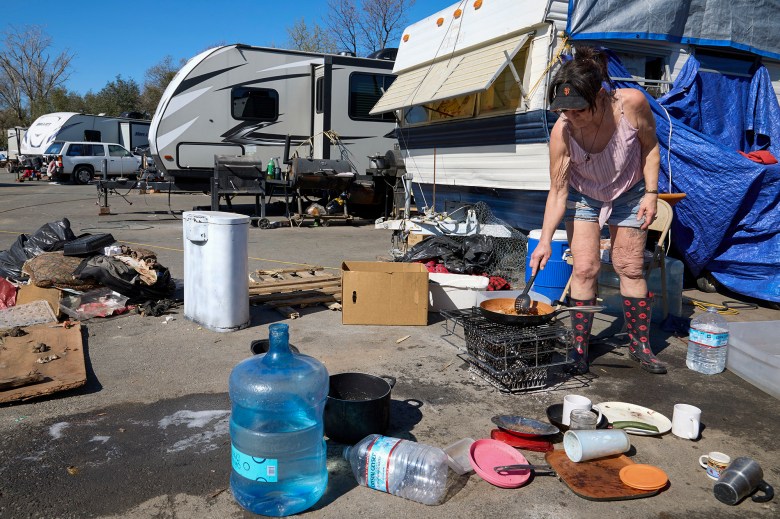 Jeanne Gillis cooks ground turkey over a wood fire next to her trailer at Camp Resolution on Feb. 28, 2024. Residents must rely on bottled water, generators, and wood fires because no utilities are provided at the camp. Photo by Fred Greaves for CalMatters
