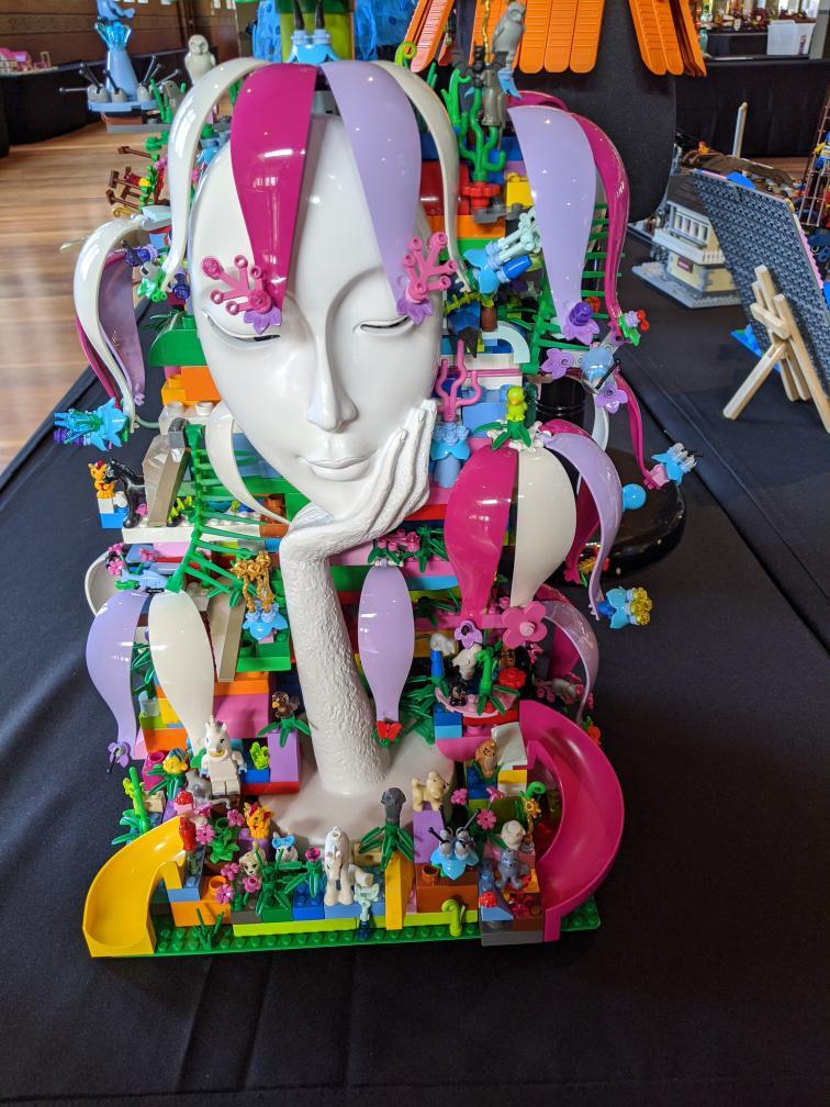 A photo of the LEGO creation "Mother Earth" by Veronica Young, depicting a sculpture of a woman's face and hand surrounded by colorful LEGO parts