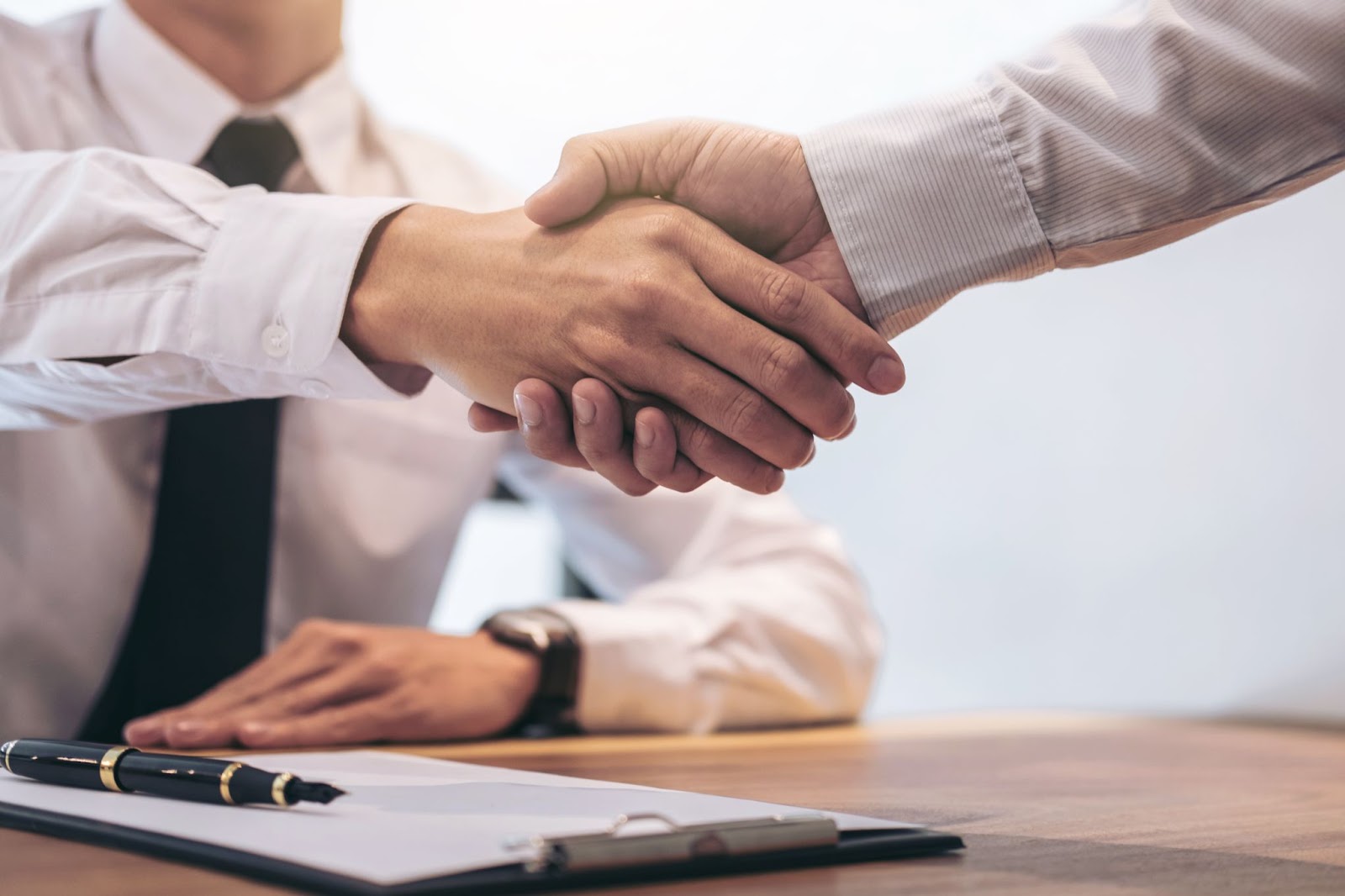 Two business professionals shaking hands across a desk in an office setting.
