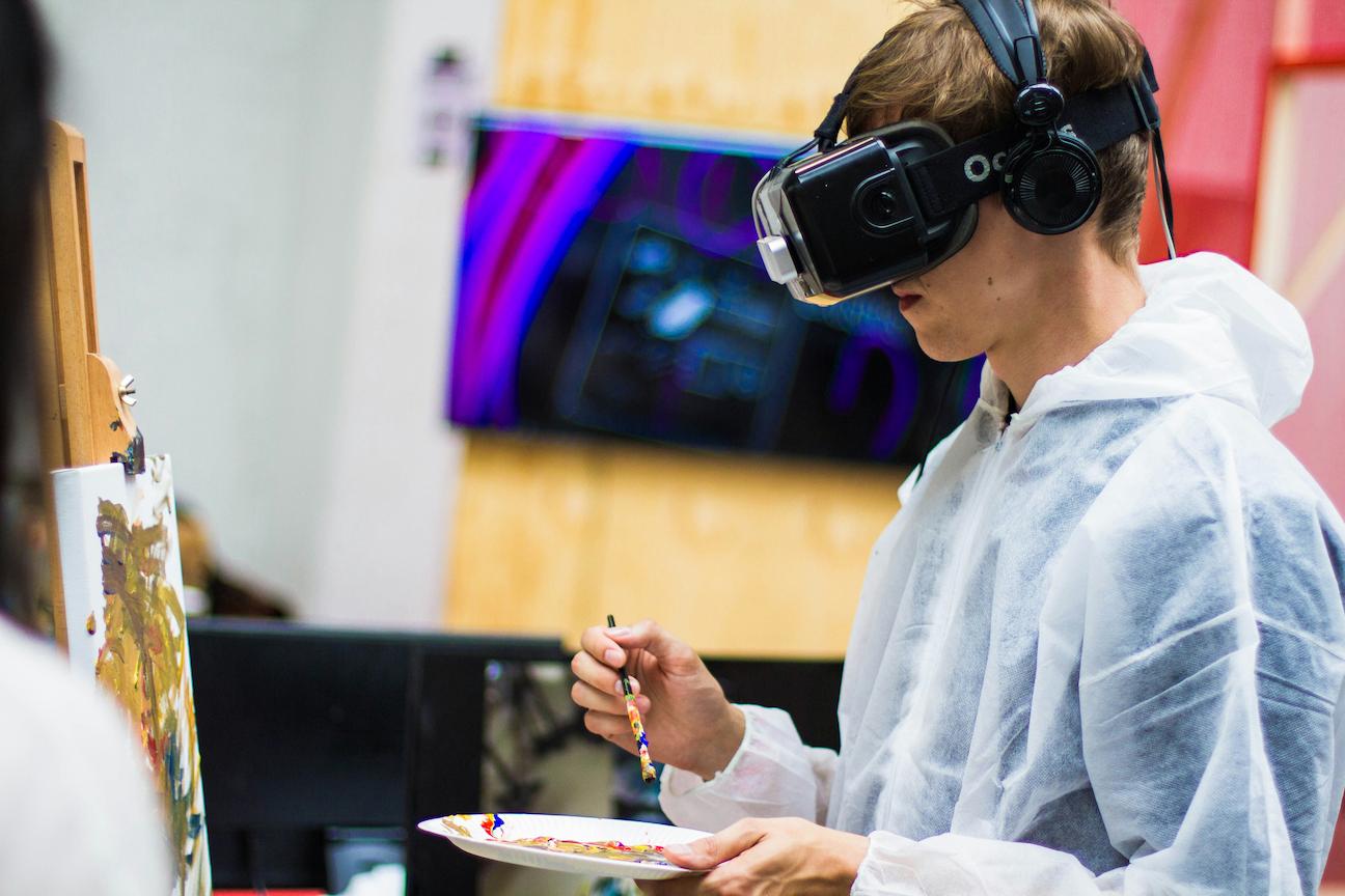 A male student wearing a device on his head, like goggles while painting.