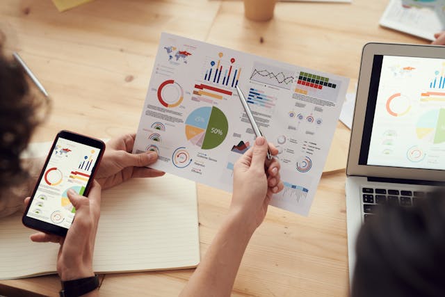 Person holding laptop and phone displaying graph.