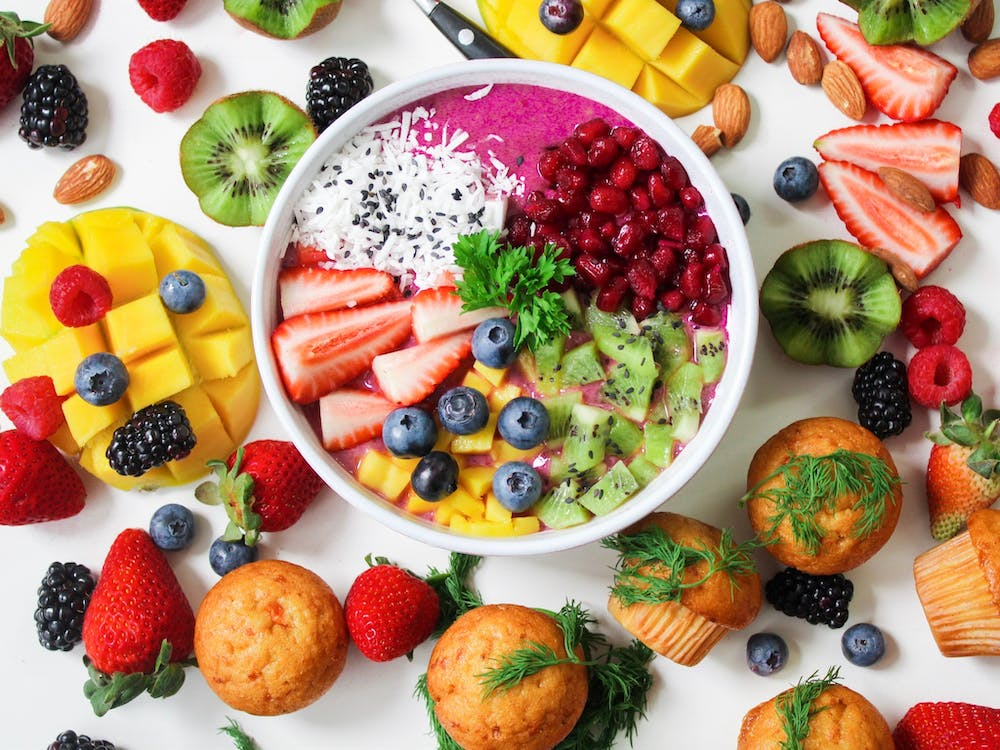 a bowl of fresh fruit surrounded by lot of different fruits and cupcakes