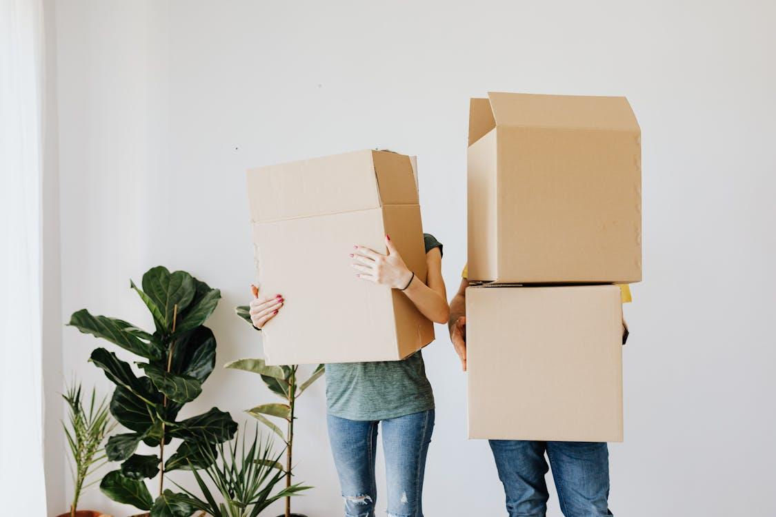 Free Unrecognizable couple wearing jeans standing carrying stacked carton boxes out of apartment during renovation on daytime Stock Photo