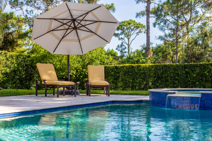 A beautiful backyard swimming pool with two chairs and an umbrella nearby.