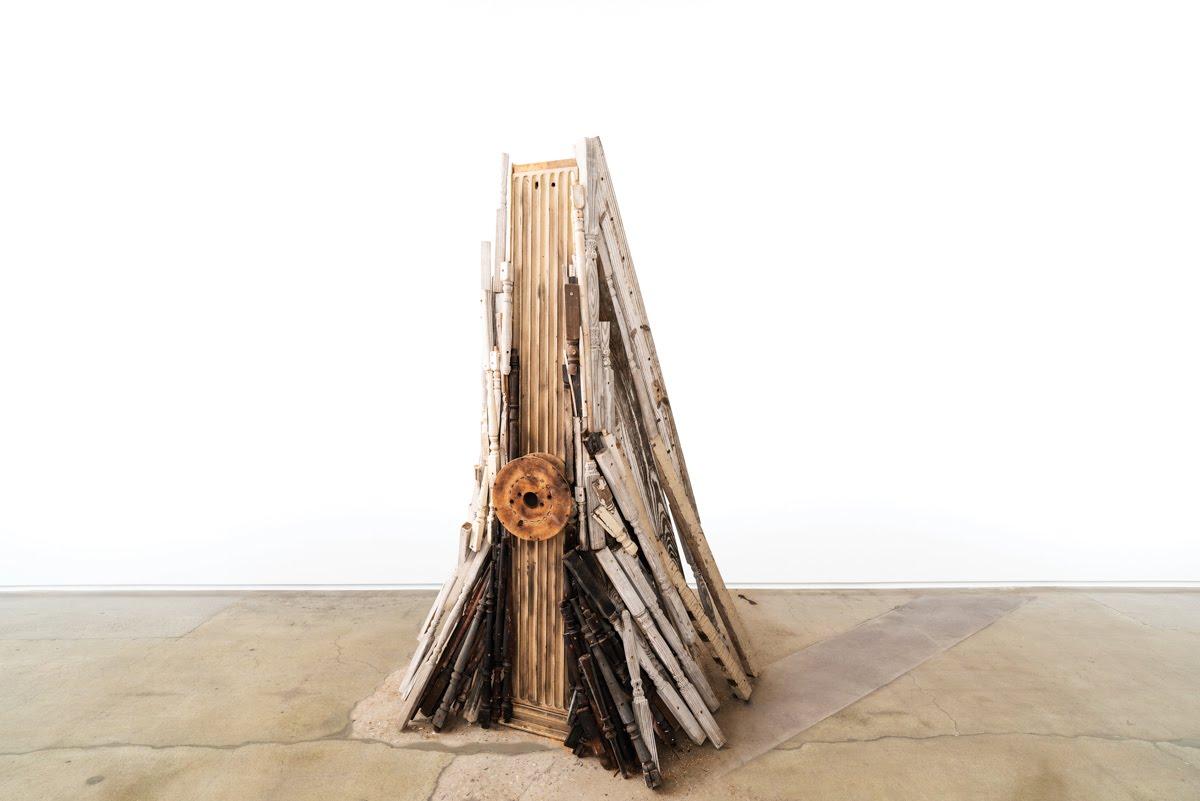 An assemblage made of wooden dowels, the kind that support railings, forms a pyramid-like shape.
