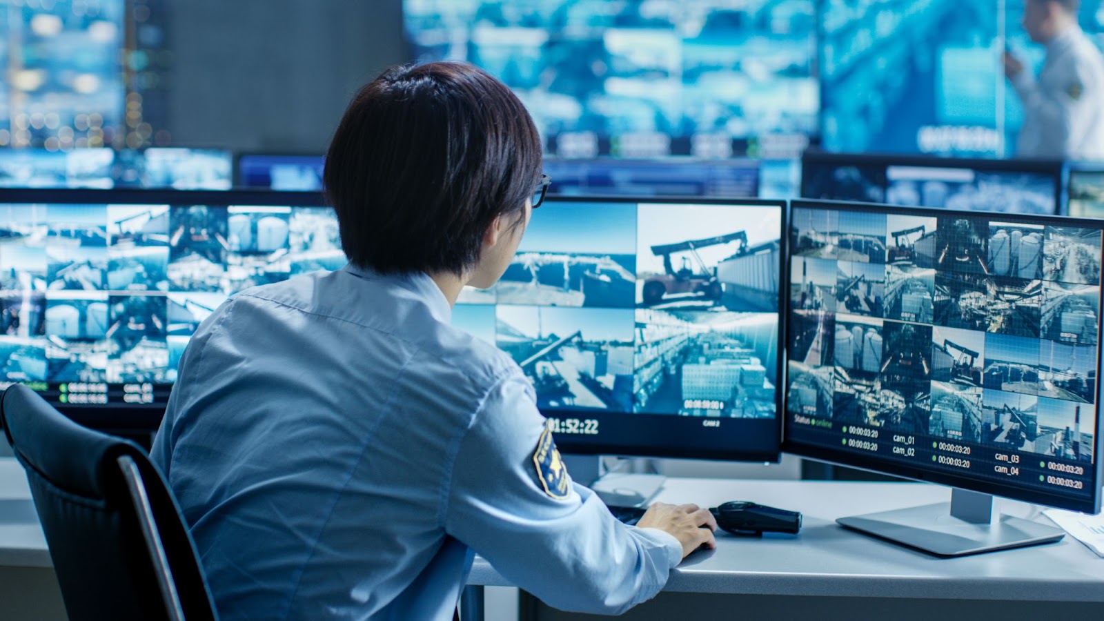 Personnel de sécurité contrôlant plusieurs flux de surveillance sur des écrans d'ordinateur dans une salle de contrôle.