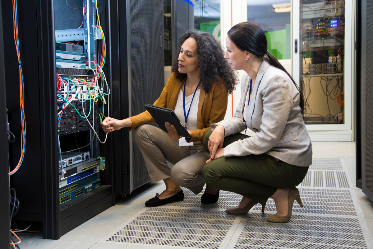 imagem ilustrativa com 2 mulheres mexendo em cabos de sistemas de TI fazendo parte da alocação de profissionais de TI  1