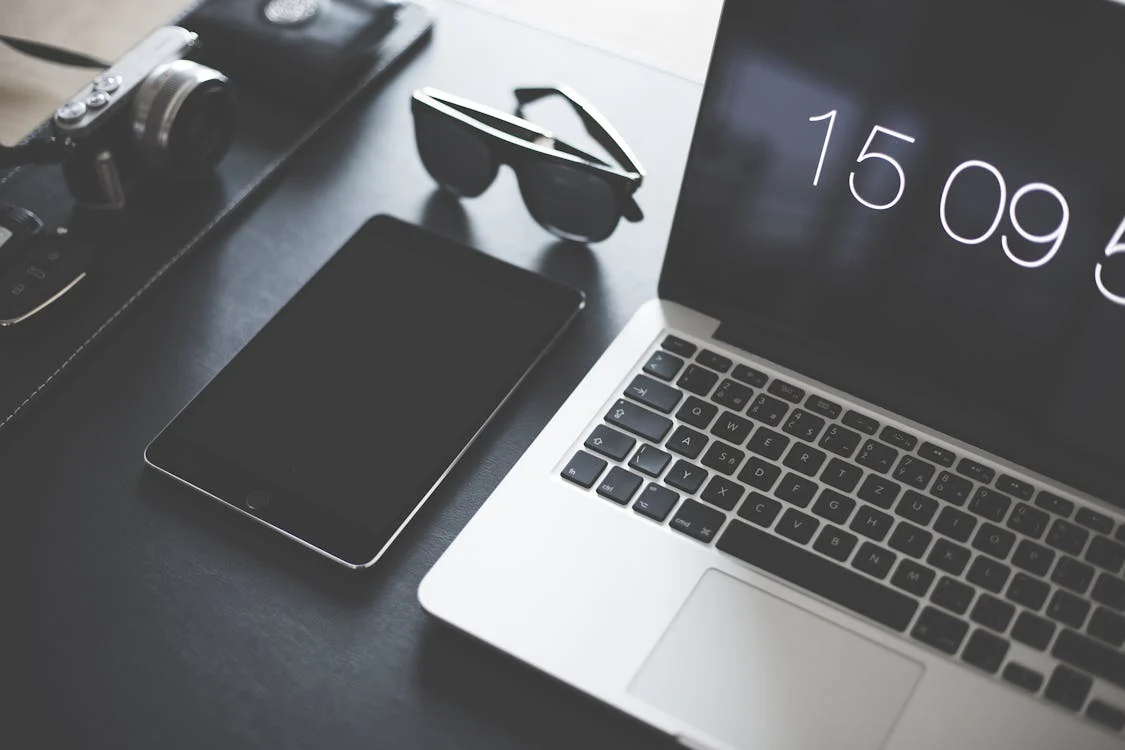 A laptop and iPad next to a pair of sunglasses