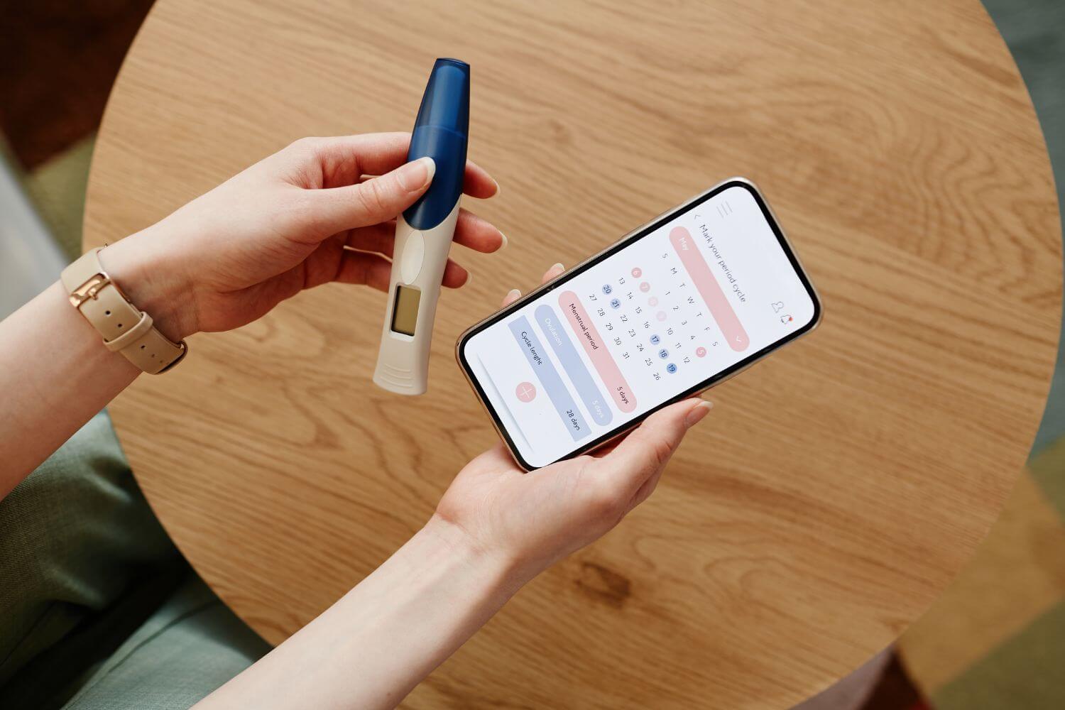 woman holding a pregnancy test and a phone showing an ovulation tracking app