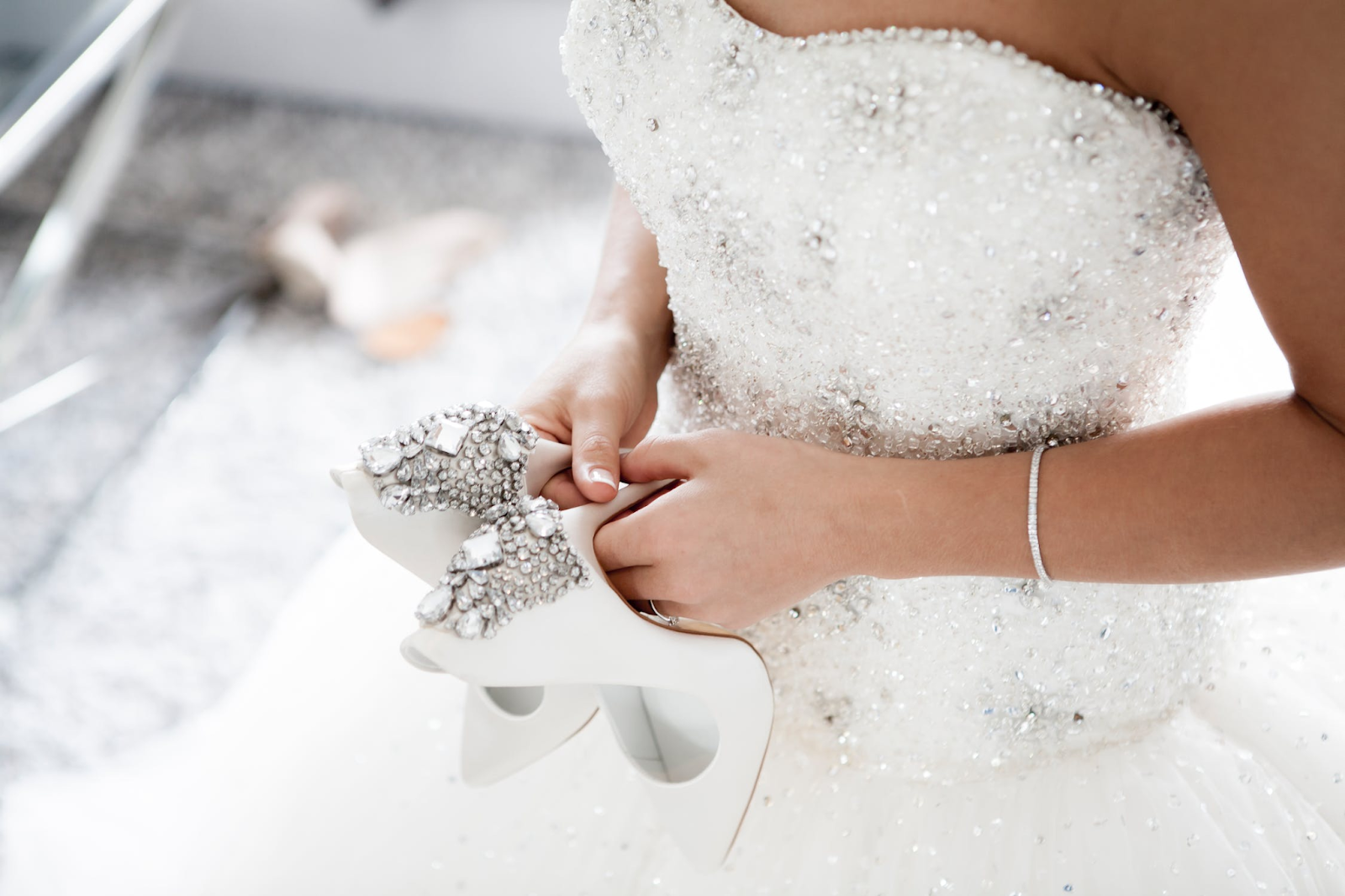 Bride in a beaded wedding dress holding embellished white high heel shoes