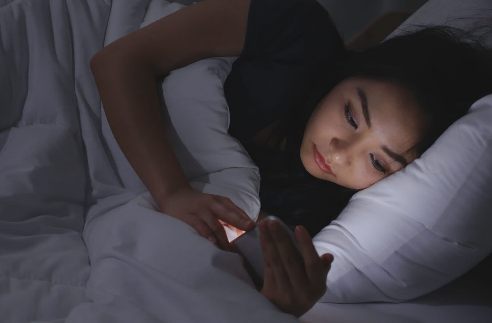 A woman using her phone while lying down in her bed.