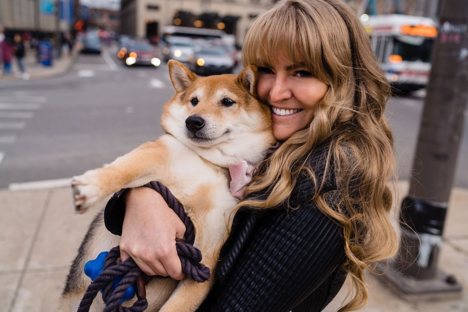 Ashley hugs her dog closely on the sidewalk of a busy city street