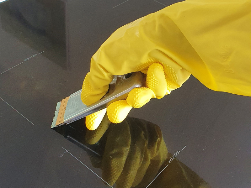 Čistenie varnej dosky so škrabkou v ruke v žltej rukavici.