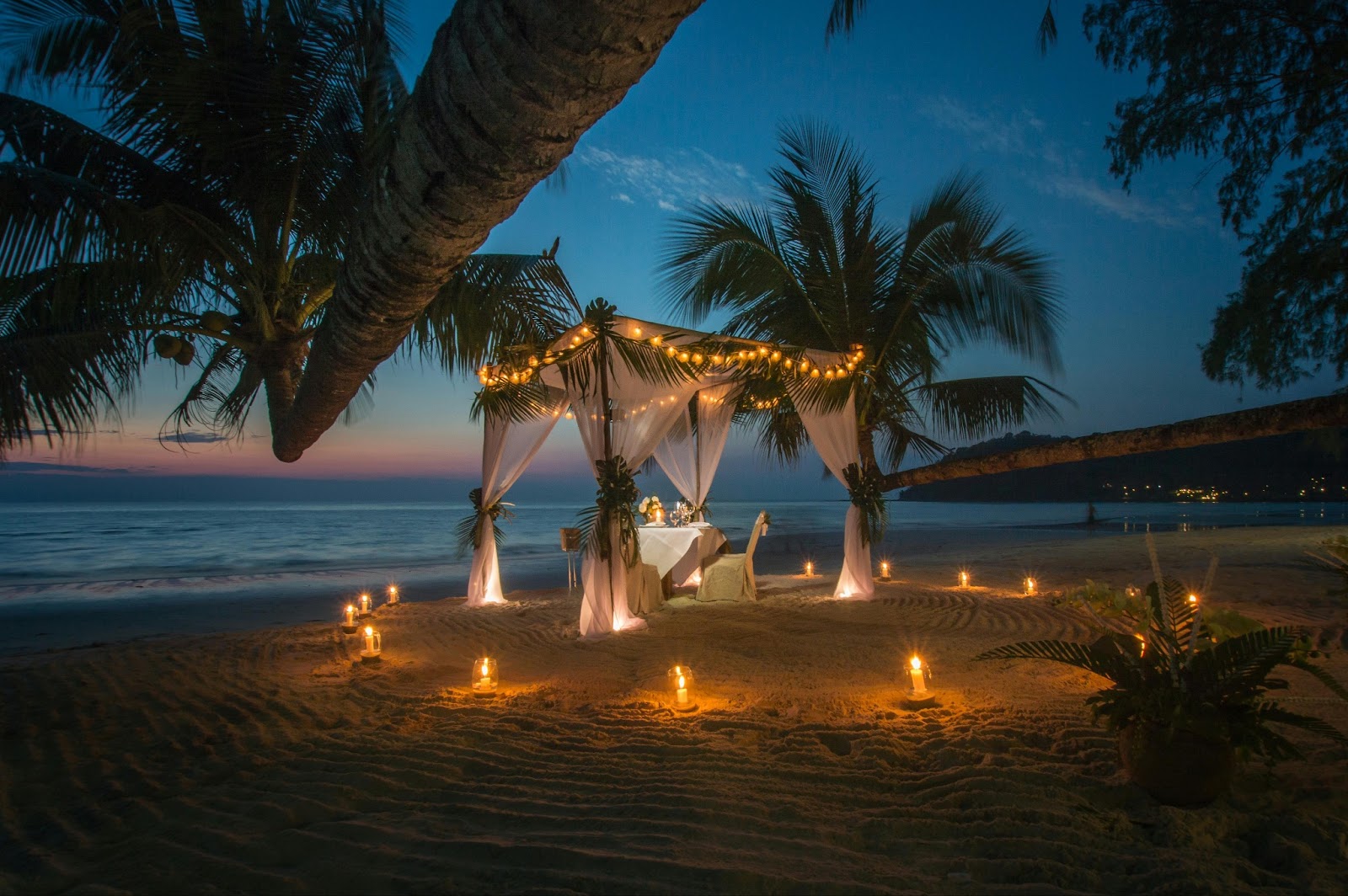 A couple enjoying a romantic candlelit dinner on the beach at sunset.