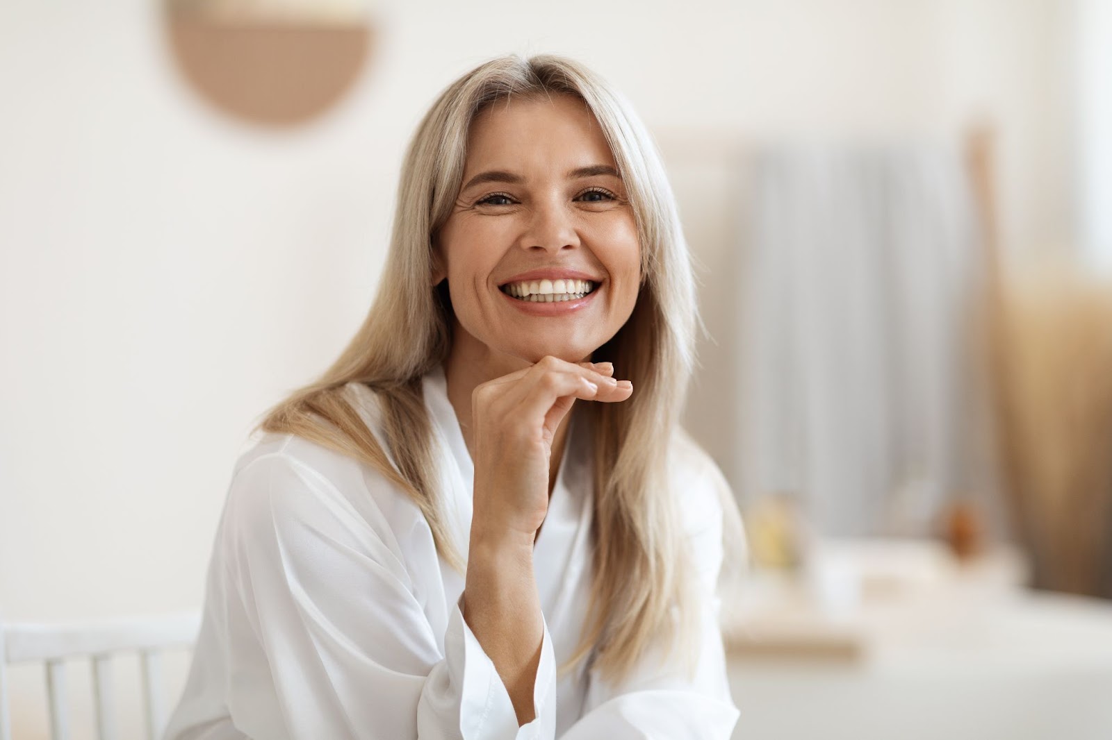 Happy middle-aged woman sitting down on a chair and smiling at the camera